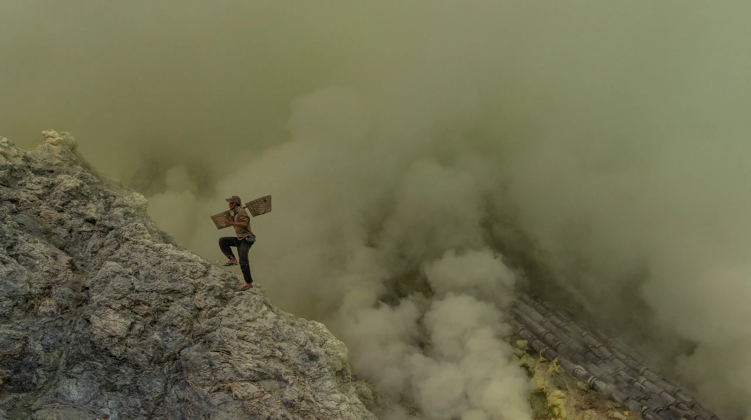 A sulfur miner climbs out of the Ijen crater through the smoke